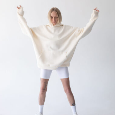 Beautiful blonde woman posing in white hoodie and leggings posing against white background