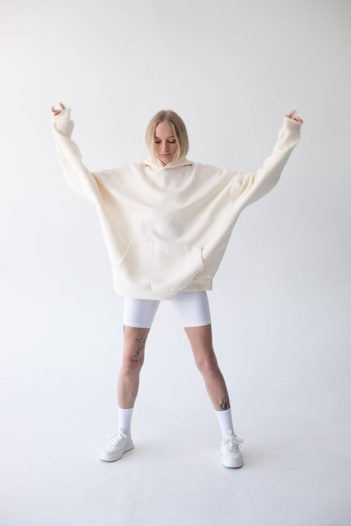 Beautiful blonde woman posing in white hoodie and leggings posing against white background