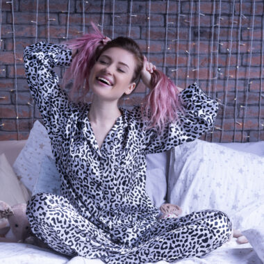 Funny woman sits on the bed in leopard pajamas and smiles