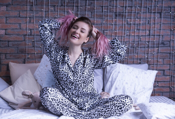 Funny woman sits on the bed in leopard pajamas and smiles