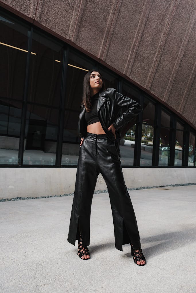 Fashionable woman in a leather jacket confidently posing outside a modern building.