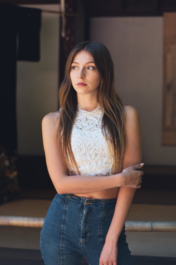 Fashionable woman posing indoors in embroidered blouse and jeans, exuding elegance and style.