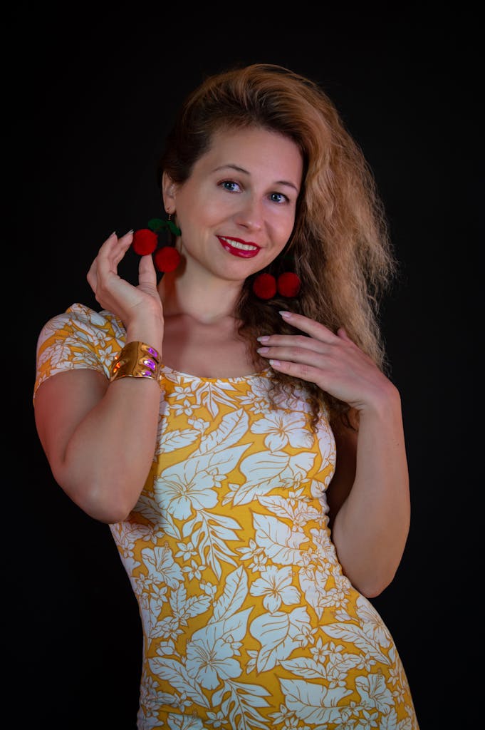 Smiling woman in a bright floral dress accessorizing with bold red earrings and bracelet.