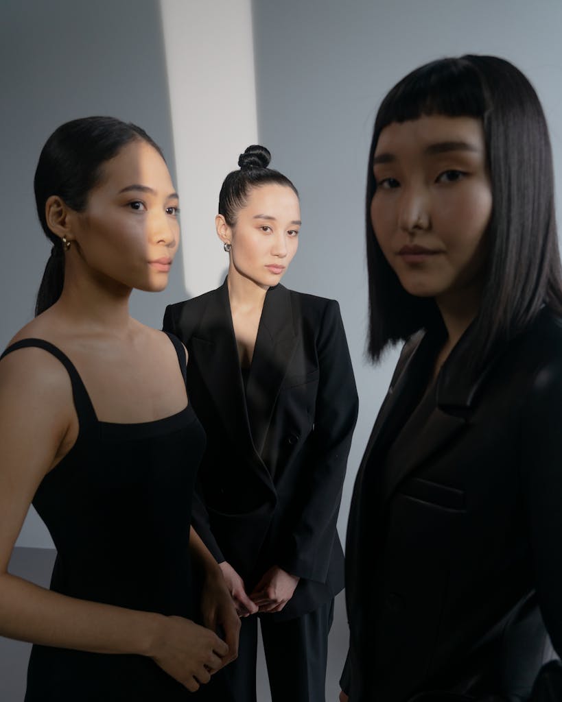 Three stylish Asian women posing in sleek black attire in a studio setting, embracing modern fashion.